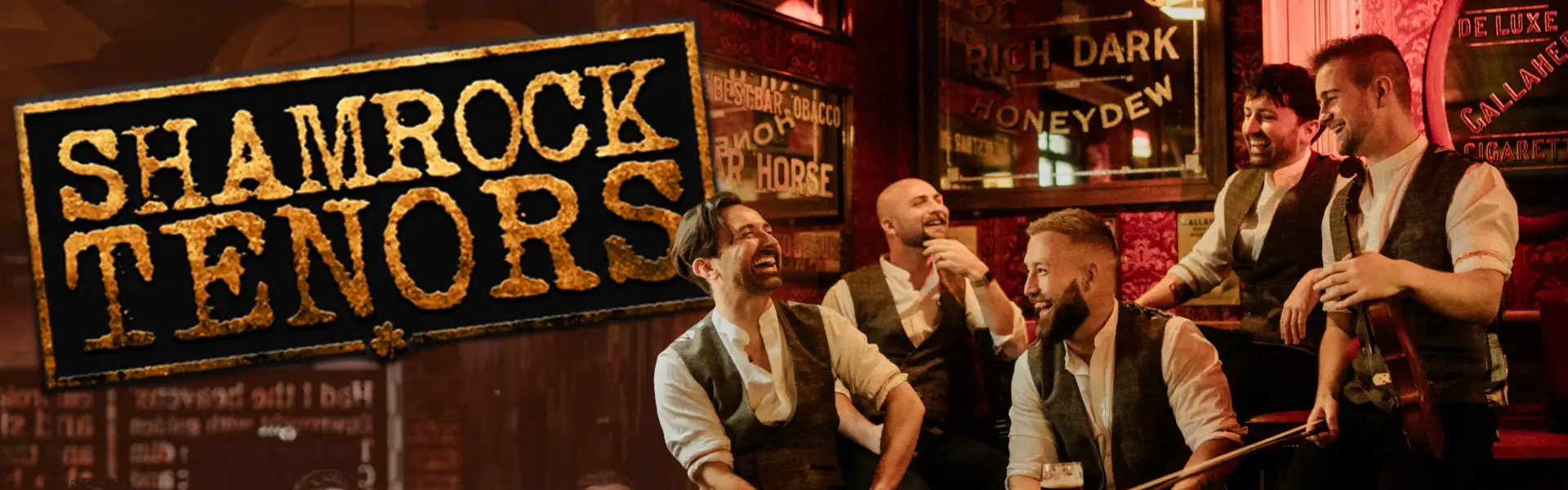Promotional image for the Shamrock Tenors, featuring the group of five men dressed in vests and white shirts, laughing and holding drinks in a cozy pub setting, with the group's name in a rustic, textured font on the left.